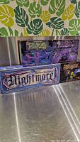 Four VHS board game boxes with horror themes displayed, showing the 'Nightmare' title and artwork including a zombie, bats, skulls, and a gothic font. The boxes rest on a metallic surface with a green and yellow leaf pattern wallpaper in background.