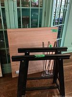 Butcher block wood top leaning against a wall with the metal hairpin legs and saw horse wooden legs adjacent to it.