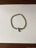 Silver ankle chain anklet with decorative small circular charms and dangling bells on white background.