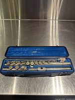 Three flute sections (headjoint, body, footjoint) arranged in open blue velvet-lined case on stainless steel surface