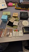 Assorted jewelry boxes, card holder, decorative pins, and fabric pouches arranged on desk