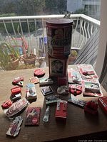 Top view showing all 22 Coca-Cola magnets arranged on a wooden table near a window, with a Coca-Cola branded tin container included.