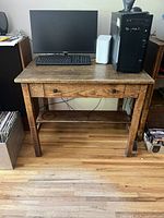 Full front view of antique solid wood desk with computer and keyboard on top, showing drawer and lower shelf.