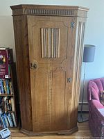 Closed view of antique wooden armoir showing carved door detail and metal hardware.