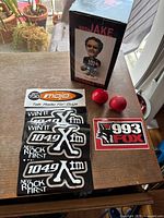 Photo of Bro Jake bobblehead box, red antenna bobbles, and radio station stickers on a wooden surface.