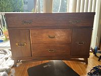 Front view of brown wooden drawer cabinet with metal handles on two side compartments and three central drawers.