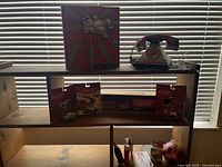 Shelf with Coca-Cola vintage rotary phone and Coca-Cola truck model box on top shelf, two Coca-Cola die-cast car models in sealed packaging on middle shelf.