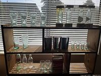 24 Coca-Cola glassware items on two shelves including multiple classic contour glasses, shot glasses, miniature bottles, and collectible bottles in boxes