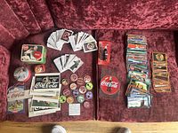 Full view of the Coca-Cola trading cards and memorabilia including tin box, buttons, and clock on red velvet upholstery.