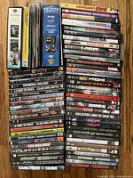 Collection of 51 DVD movies laid out showing titles and box set inclusion. Visible titles include a mix of action and thriller movies, some with French and English languages noted on spine.