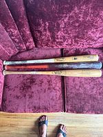Three wooden baseball bats on maroon fabric couch, showing overall condition and color variations.