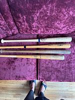 Four used wooden baseball bats laid on a purple fabric surface, showing varying wear.