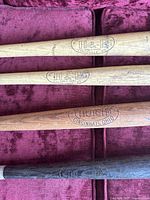 Four wooden baseball bats laid side by side showing brand stamps and wood grain.