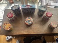 Overhead photo of 8 Coca-Cola vintage advertising tins on wooden surface, showing varied shapes and sizes with colorful retro branding