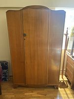 Front view of a brown wood vintage armoire with a single door and a curved top edge.