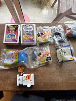 Nine vintage McDonald's Happy Meal toys displayed on a table, packaging includes Disney VHS covers and sealed plastic bags with various toys including Hot Wheels cars and Disney figures.