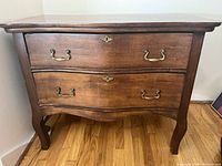 Front view of vintage wooden antique dresser showing two drawers with metal handles and curved legs on wood floor.