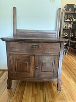 Front view of vintage wooden cabinet showing drawer and double doors, brown finish, wood grain, and handles.