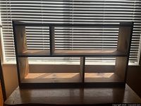 Front view of the wooden shelf showing four compartments against window blinds