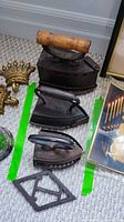 Top view of three different antique cast iron irons and one cast iron T. Eaton Company trivet on carpeted floor.