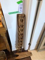 Full view of both the long maple sugar candy mold with heart shapes and the wooden boot jack on the floor leaning against a wall.