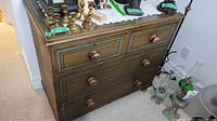 Front and top angle photo of dresser showing four drawers with dovetailed joints, wooden knobs, and worn finish. Several brass and metal decorative items rest on top (not included).