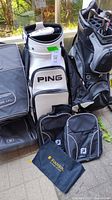 Wide view of Ping golf bag with four FootJoy shoe bags placed in front and to the side, shown on a patio area with grass in background.