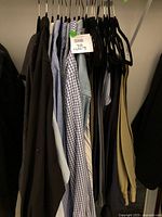 Photo showing a rack of men's clothing including various shirts (solid, checked, denim) and pants on hangers