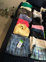 Overview photo showing folded men's sweaters, golf shirts, and multiple pairs of shorts laid out on a bed, showcasing colors, patterns, and brands