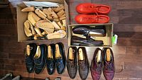 Overview photo showing multiple pairs of men's dress shoes arranged on floor beside box filled with wooden shoe trees