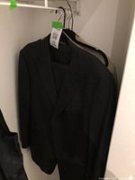 Three men's suits hanging on hangers. Front suit is black, wrinkle marks visible, other two suits partially visible behind.