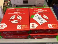 Four unopened packages of Staples copy paper stacked together, showing front packaging with eco-friendly and FSC logos, 500 sheets each.