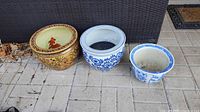 Full view of all three Asian themed porcelain plant pots placed on a tiled floor, showing different sizes and designs.