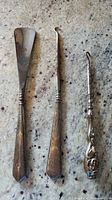 Photo showing antique shoe horn and two hooks with sterling silver handles on granite countertop.