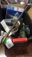 Plastic bin containing Bosch green power drill, crowbar with red handle, saw blade, and other assorted tools and parts.