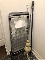 Full view of the foldable metal utility cart with wheels, the adjustable walking stick leaning against the wall, and the decorative wooden item on the floor