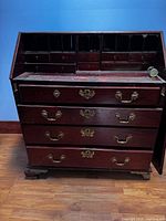 Front view of mahogany writing desk with multiple drawers and pigeonhole compartments above, showing wear and need for restoration.
