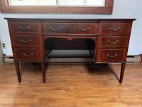 Full view of antique mahogany writing desk, showing all drawers and legs, wood finish and brass drawer handles.