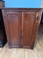 Front view of closed antique wooden storage cabinet showing two paneled doors with metal hinges and key lock.
