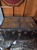 Closed antique trunk showing black finish with metal reinforcements and lock mechanism