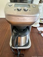 Front view of Breville coffee grinder and coffee maker with stainless steel thermal carafe and control knobs.