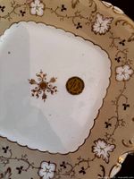 Top view of square antique china plate showing gold floral decorations and gold trim with Royal Austria mark on back
