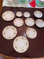 Top view of all 10 decorative china plates arranged on a wooden surface, showing floral pattern and size variations.
