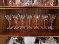 Seven clear crystal wine glasses lined up on a wooden shelf, showing their shape, size, and condition.