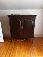 Front view of the dark wooden entertainment center cabinet with closed doors showing decorative panels and curved legs.
