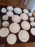 Full set of plates, teacups and saucers arranged on a table showing gold decorative trim and patterning.