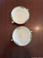 Top view of two white Japan china tea cups with floral decoration and gold handle detailing on a dark wood surface