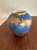 Angled photo of the round blue pottery bowl with gold leaf leaf patterns encircling the exterior.