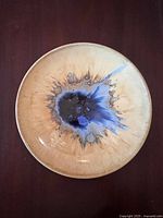Top-down photo of a circular pottery plate showcasing a unique central splash glaze pattern in blue, black, and beige with a glossy finish.