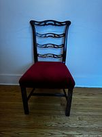 Full view of wooden chair with dark finish and red velvet seat against white wall.